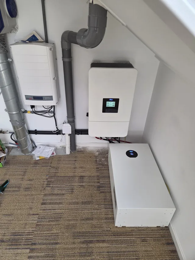 Deye inverter next to a SolarEdge inverter in an attic, with one battery module lying on the floor.